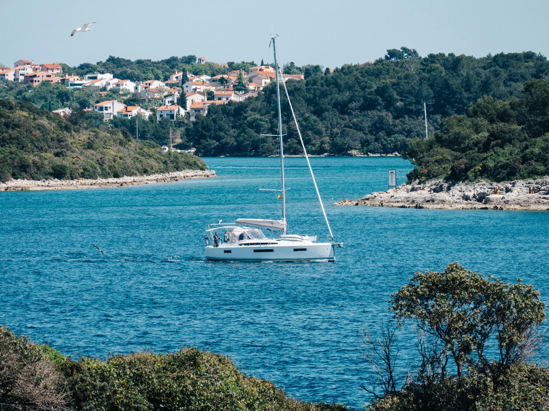 Sailing yacht under way on turquoise water in a bay along a green Adriatic coastline